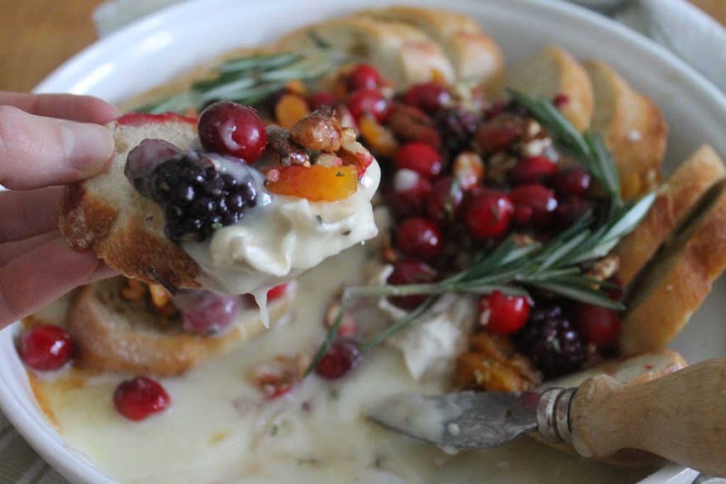 Holding a slice of toasted baguette with the baked brie dip with fresh cranberries and blackberries.