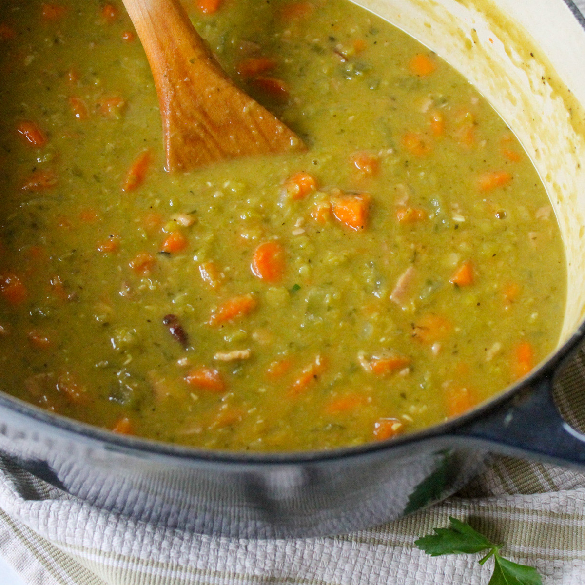 Creamy split pea soup with ham in a blue Dutch oven soup pot with a wooden spoon.