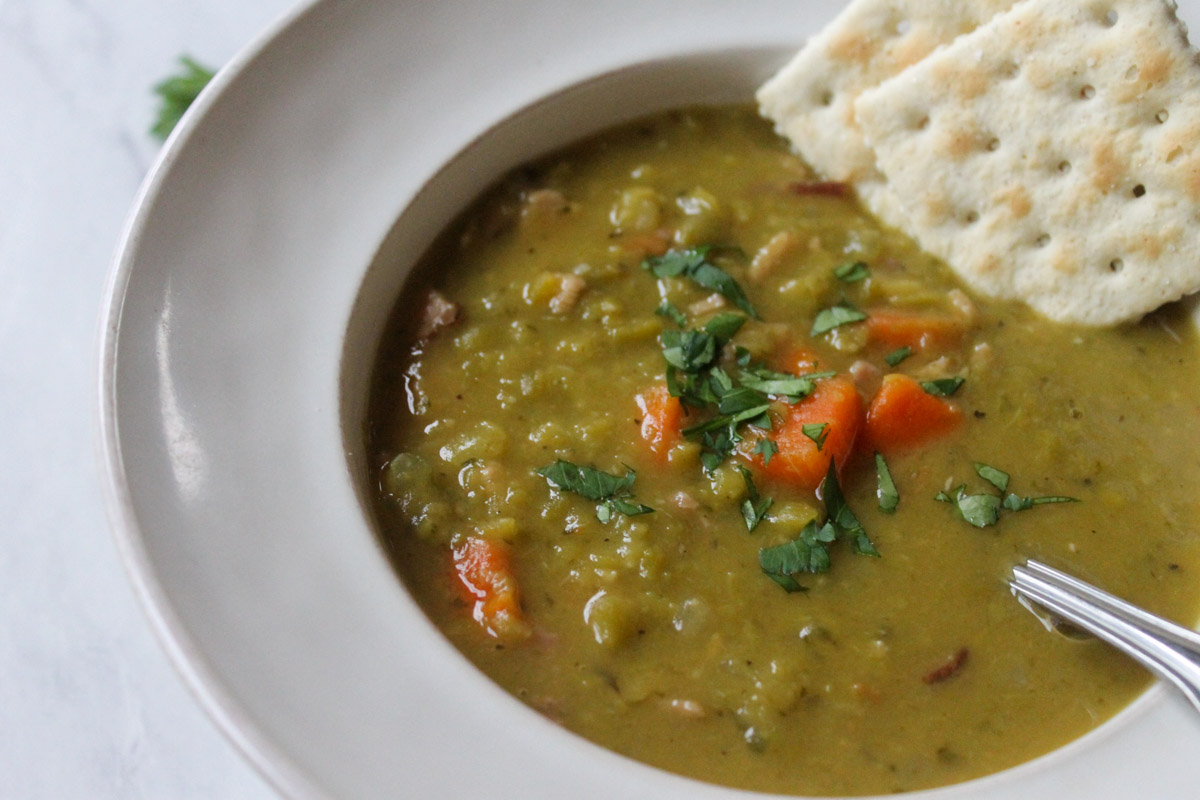 A white bowl of split pea soup with ham topped with parsley.