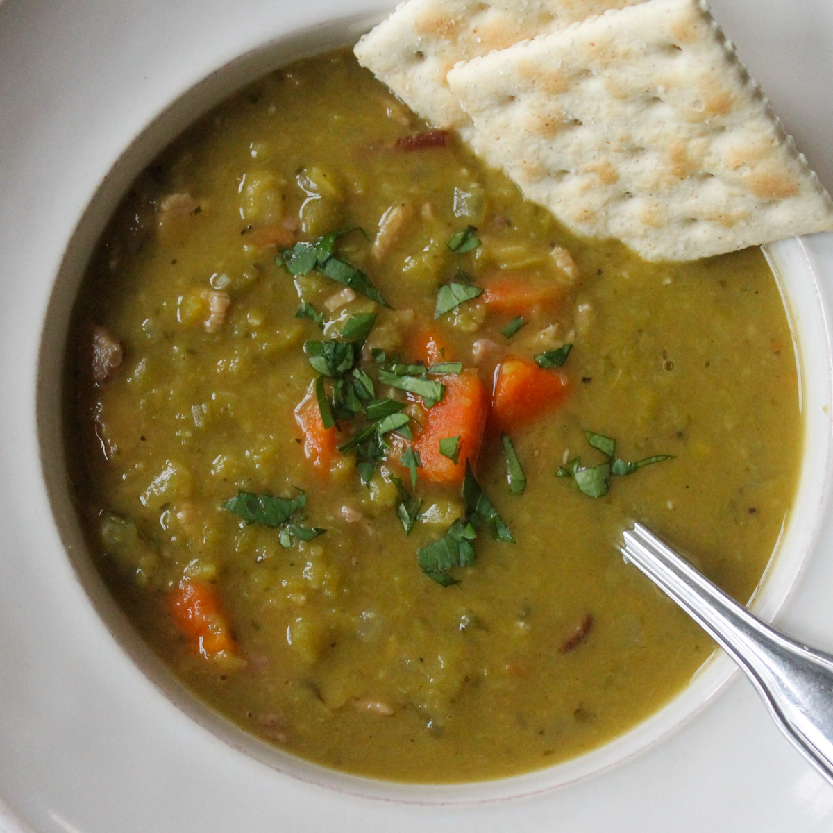 A top down close up of a bowl of split pea soup with saltine crackers.