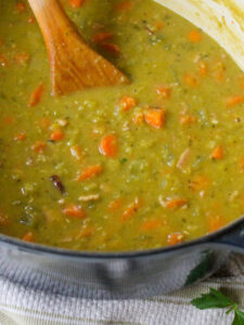 Creamy split pea soup with ham in a blue Dutch oven soup pot with a wooden spoon.