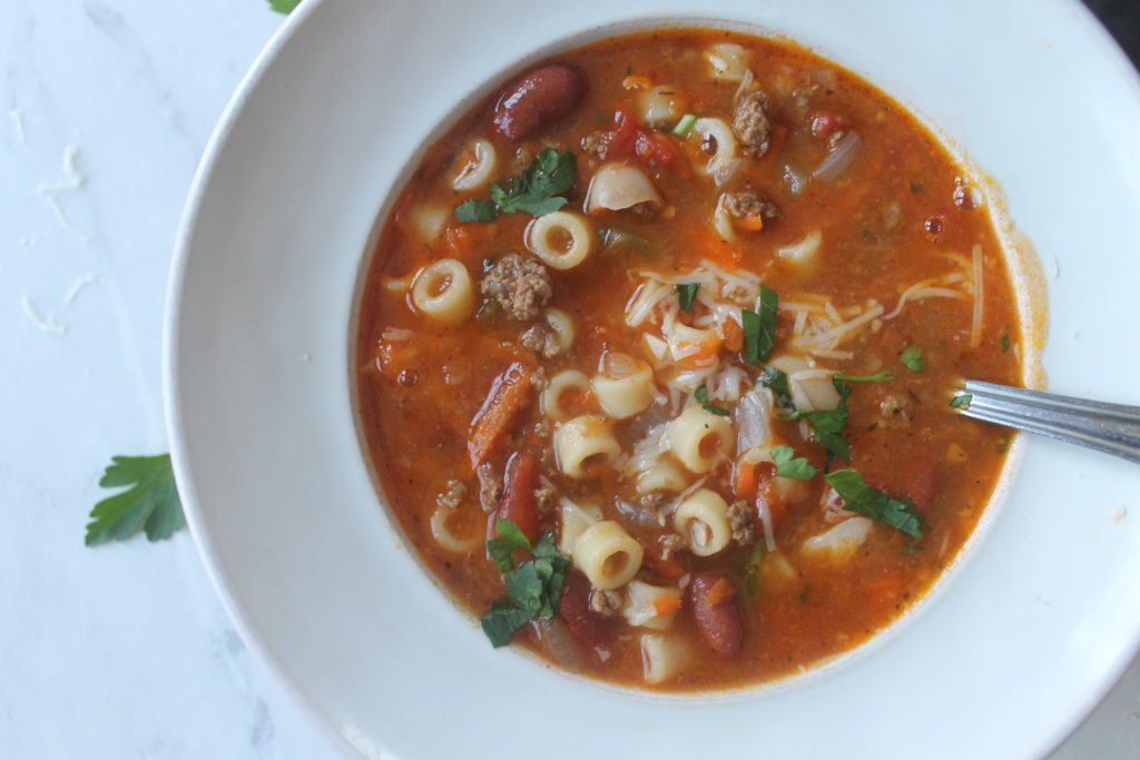 A white bowl of Pasta Fagioli Soup garnished with fresh parsley.