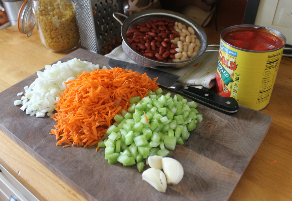Pasta Fagioli Soup ingredients prepped on a cutting board including chopped onion, celery and shredded carrots.