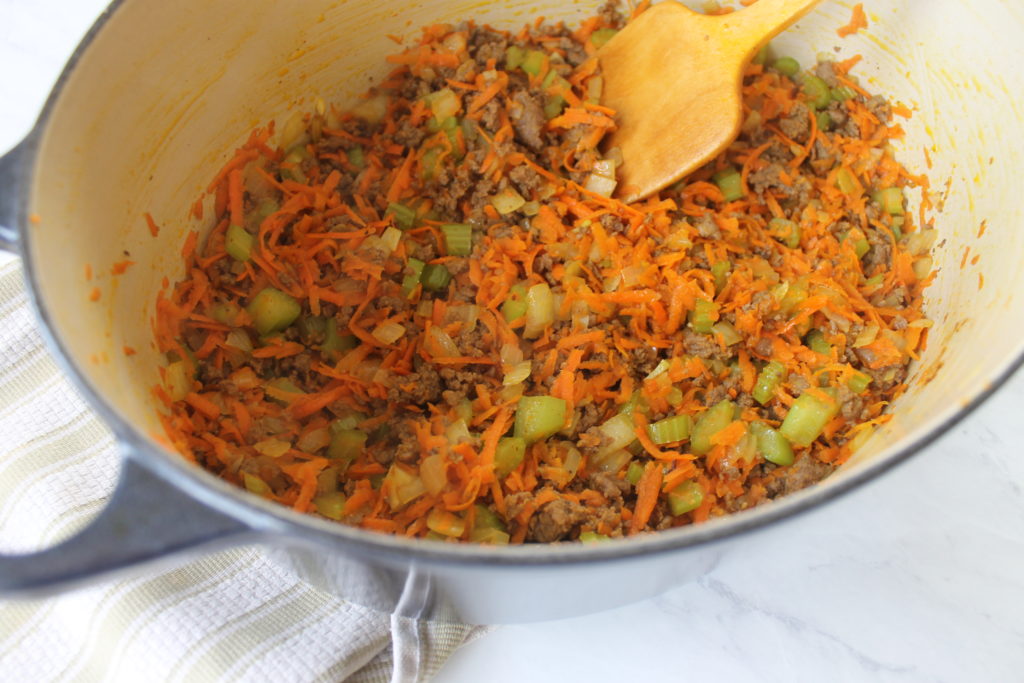 A soup pot with browned ground beef and sautéing vegetables as the base for pasta fagioli soup.