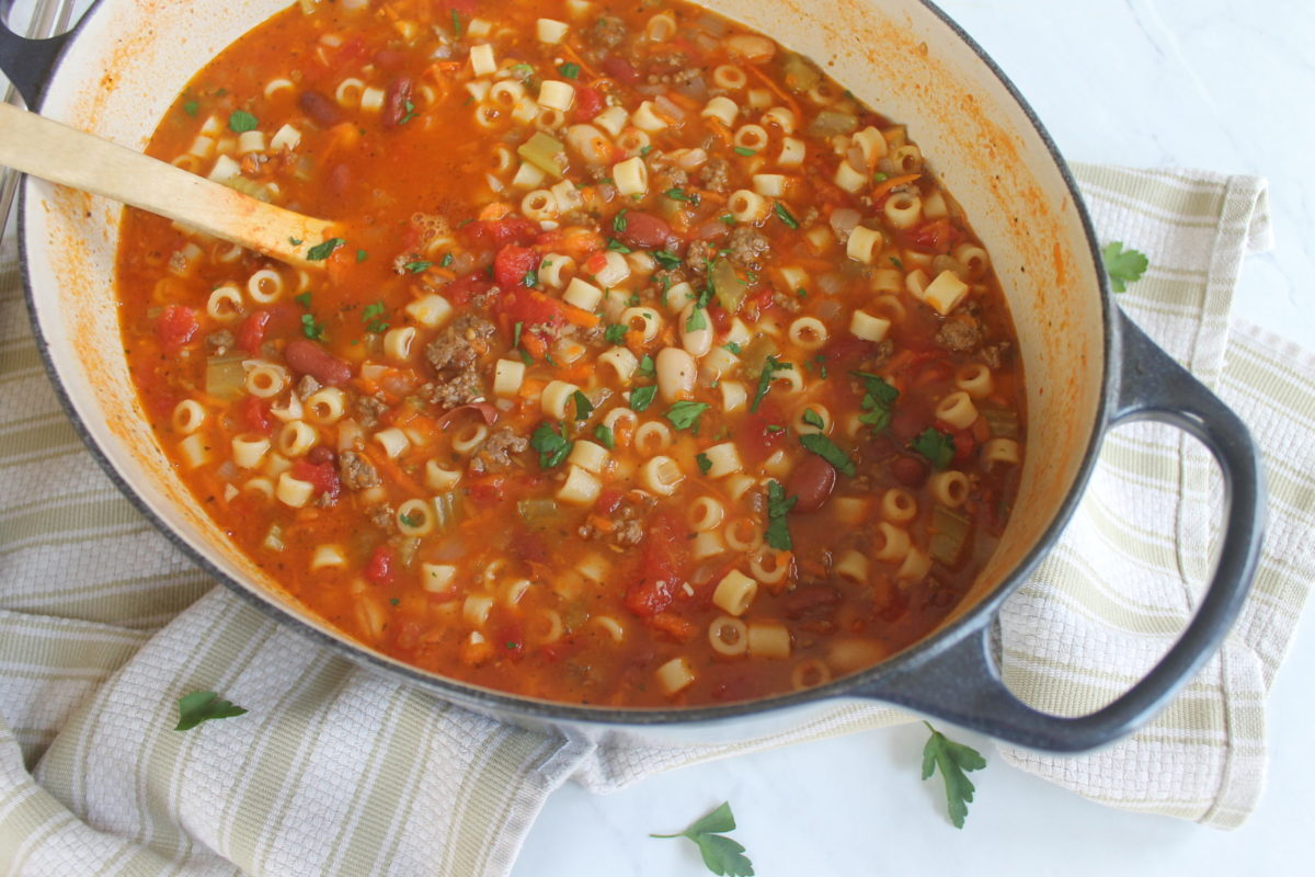 A hearty pot of Pasta Fagioli Soup full of pasta, beans, beef and veggies in a red tomato broth with a wooden spoon.