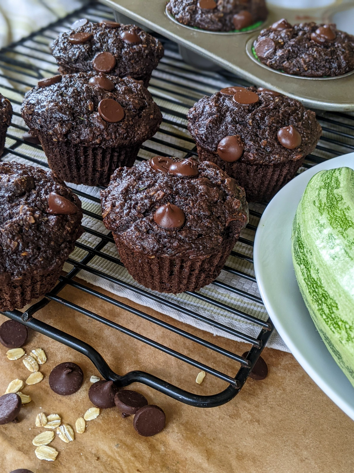 Dark chocolate zucchini muffins on a wire rack with oats and chocolate chips.