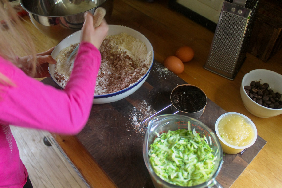 Child mixing dry ingredients for chocolate zucchini muffin batter.