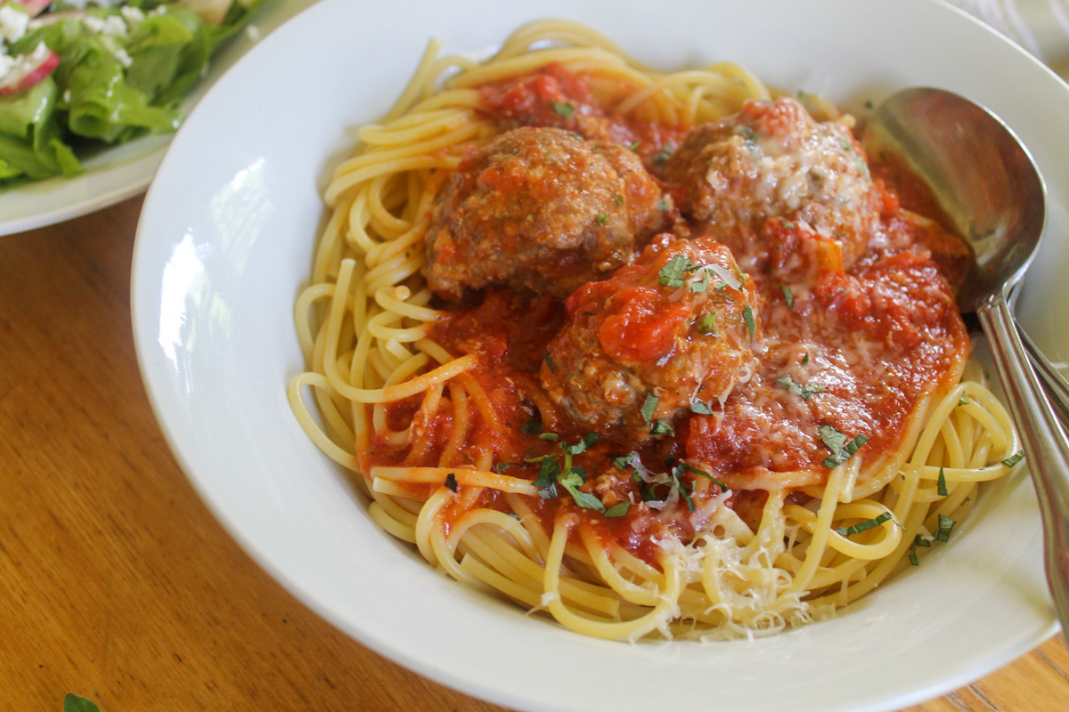 A bowl of spaghetti and meatballs topped with parmesan cheese.