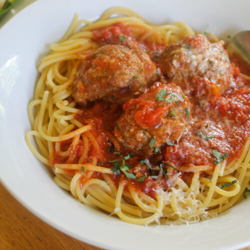 Homemade oven baked meatballs in marinara sauce over spaghetti.