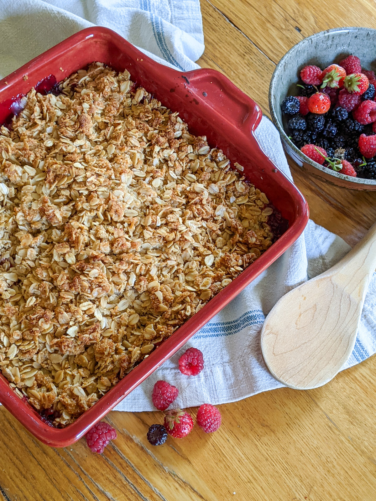 A red baking dish of baked berry rhubarb crisp with a bowl of berries.