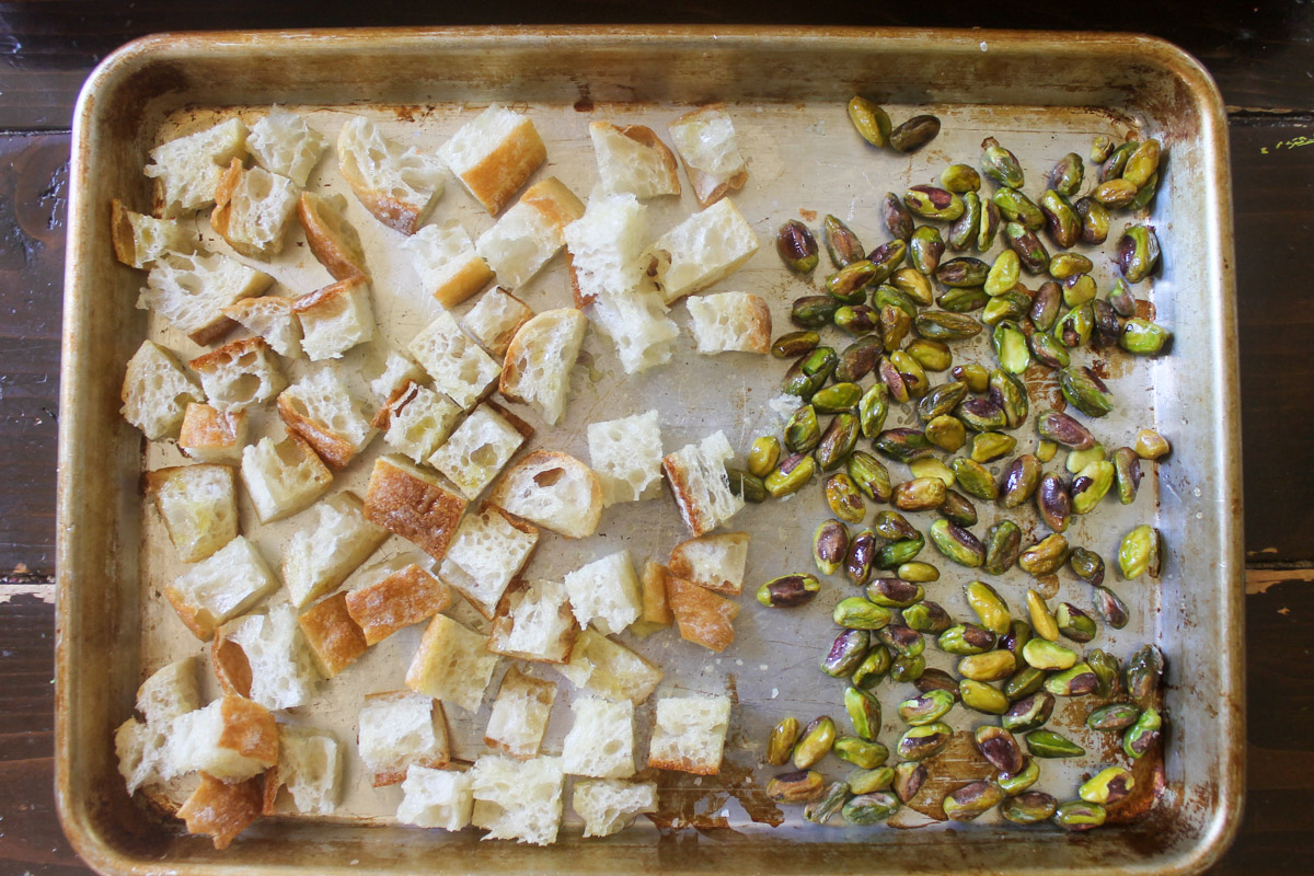 Cubed bread for croutons and pistachio nuts on a sheet pan ready to toast in the oven.