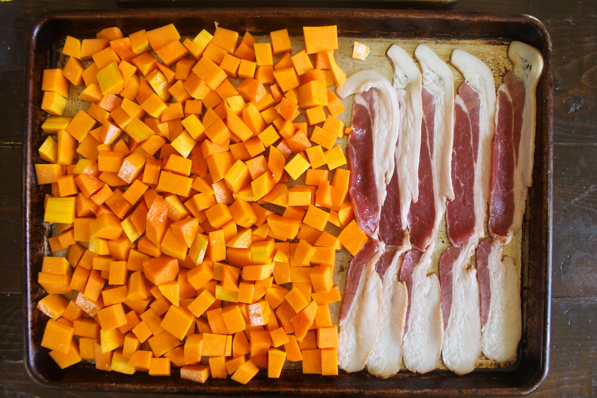 Butternut Squash cut into cubes and bacon on a sheet pan ready to roast.