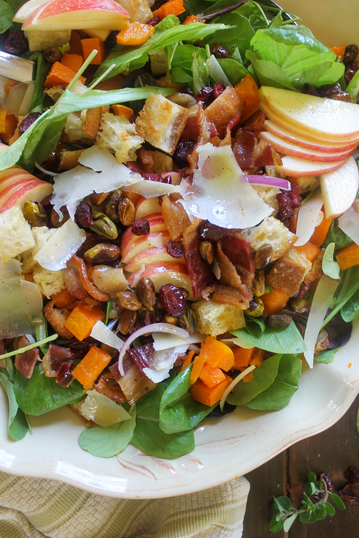 A close up of butternut squash salad with sliced apples, Parmesan cheese, dried cranberries and pistachios.