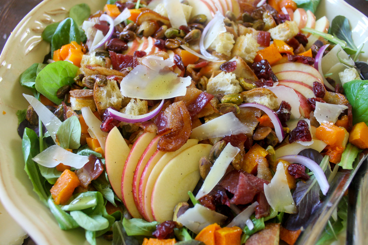 A salad with apple slices, crispy bacon, red onions, croutons and roasted butternut squash.