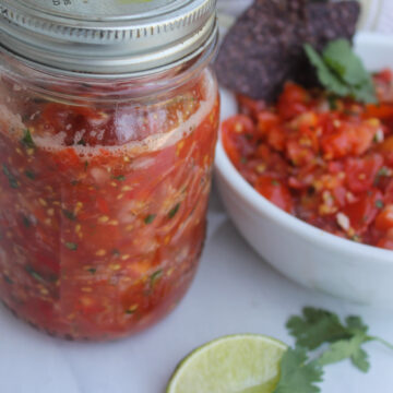 A jar of cherry tomato pico de gallo for the freezer next to an extra bowl of salsa.