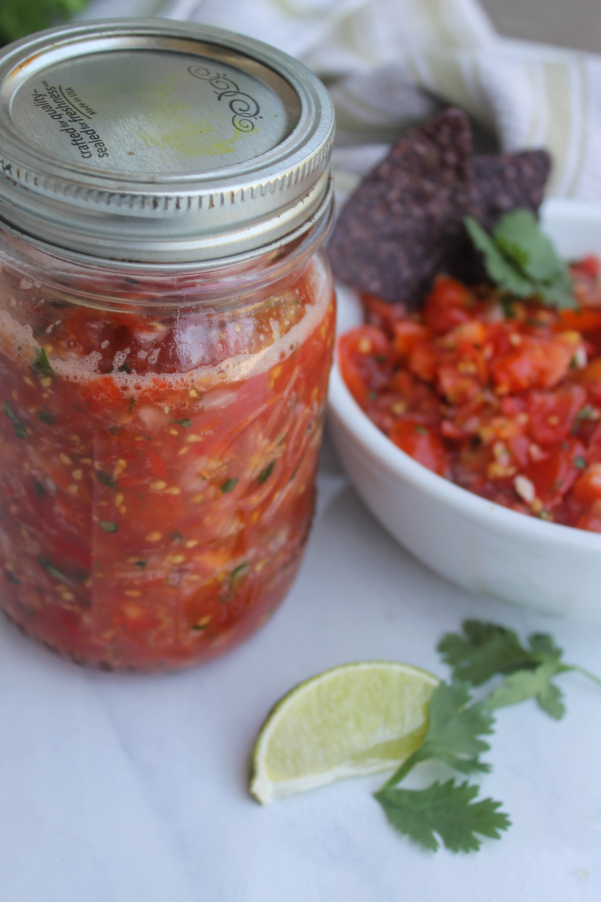 A jar of cherry tomato pico de gallo for the freezer next to an extra bowl of salsa.