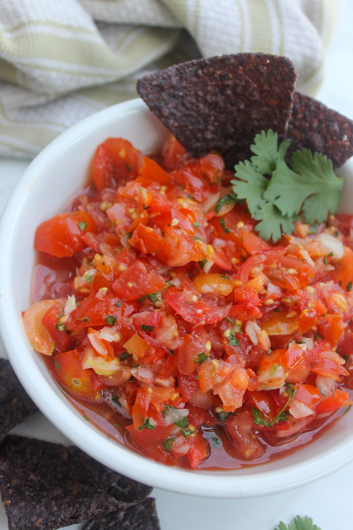 Pico de gallo using cherry tomatoes in a white bowl with blue tortilla chips.