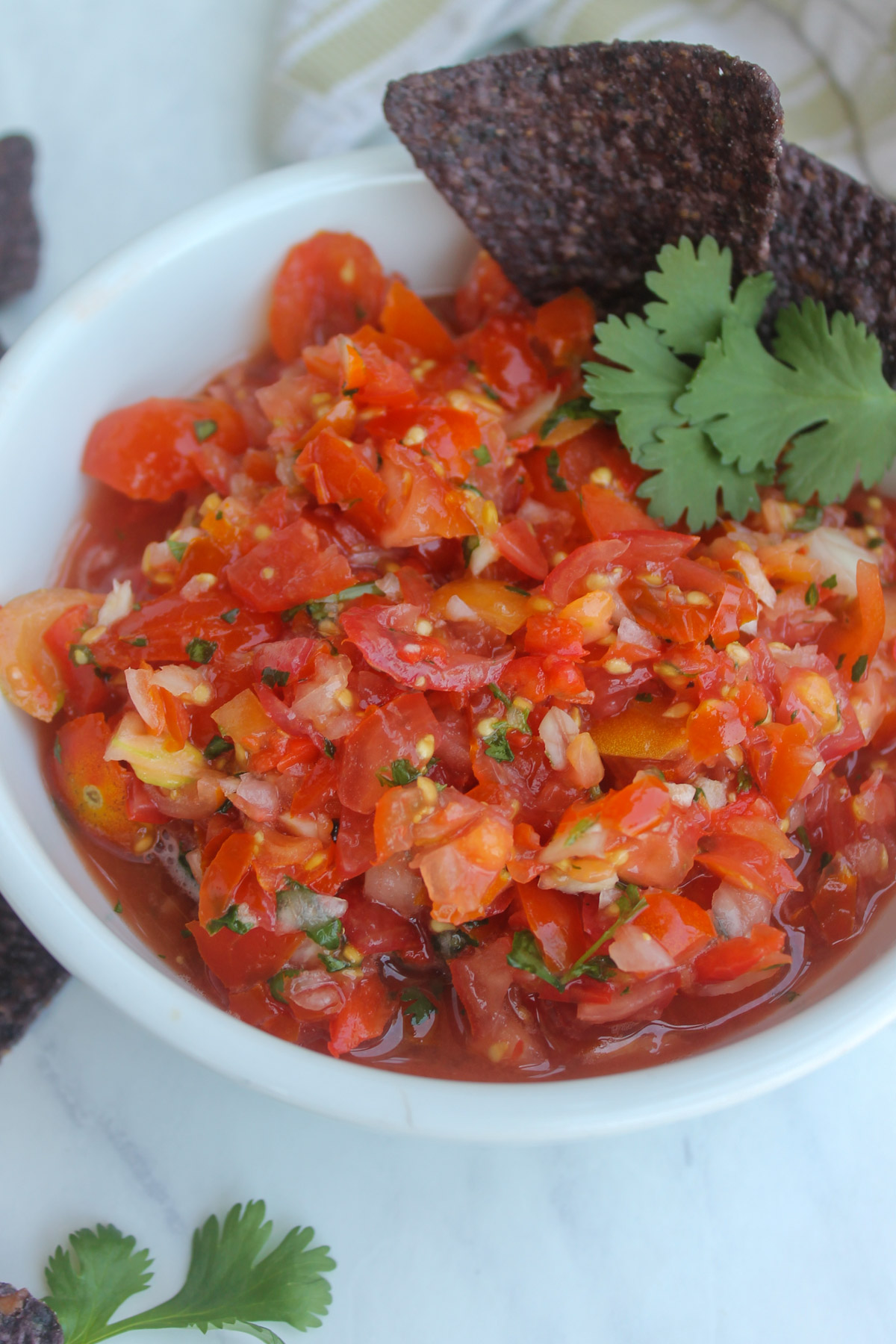 A bowl of cherry tomato pico de gallo with cilantro leaves and blue corn chips.