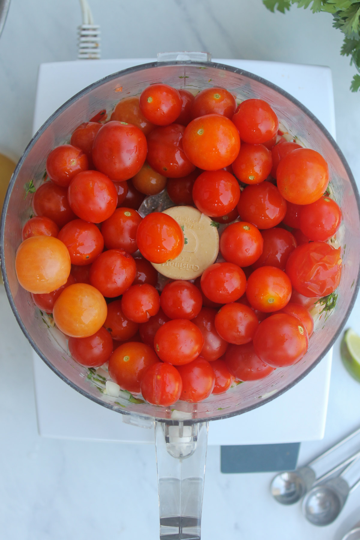 Adding cherry tomatoes to the pulsed veggies in a food processor.
