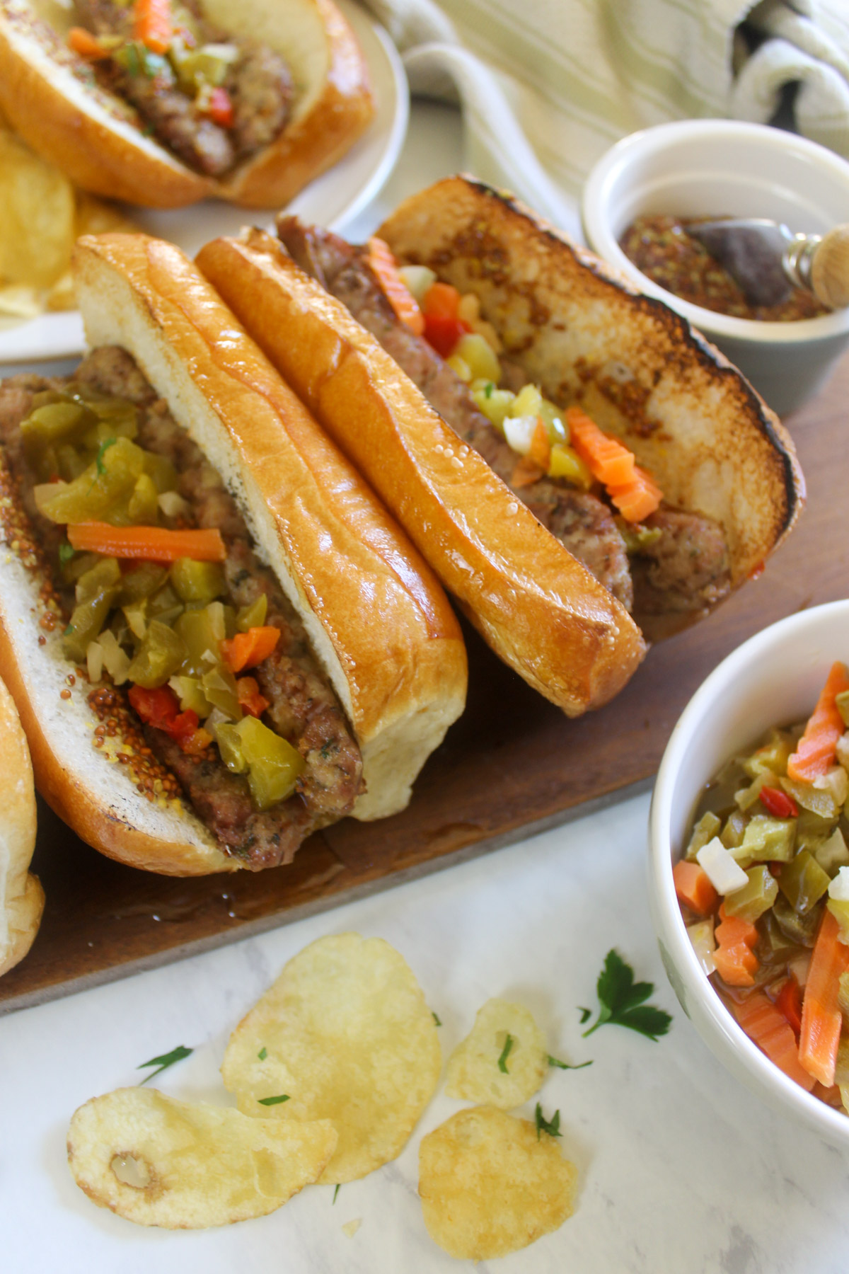 Grilled Italian sausage links in buns with giardiniera and potato chips.