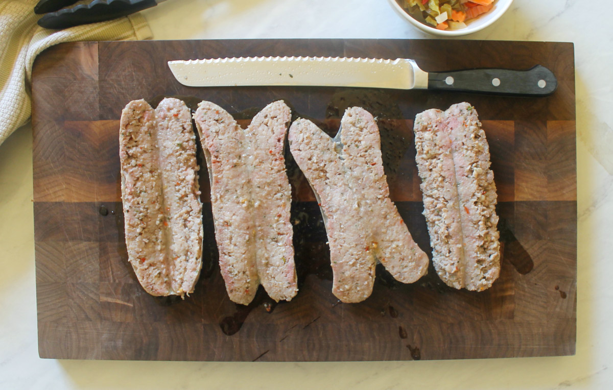 Sausage links split open on a cutting board with a serrated knife, ready to grill.
