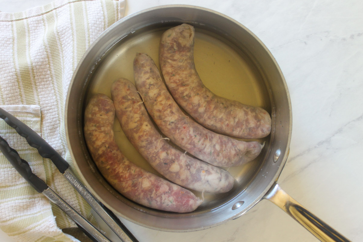 Italian sausage links simmering in a saucepan.
