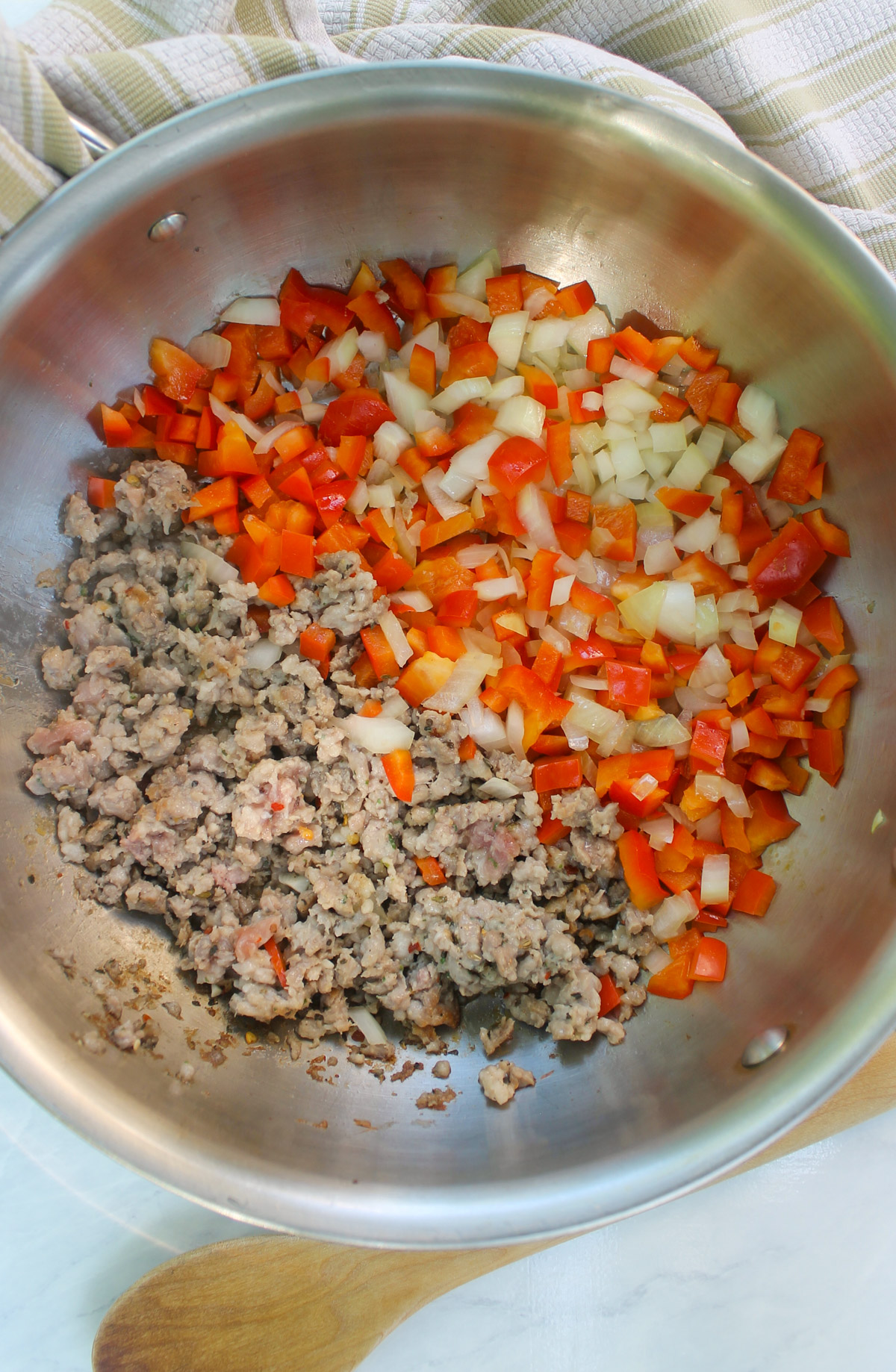 A skillet sauteing ground Italian sausage on one half and onions and red bell peppers on the other half.