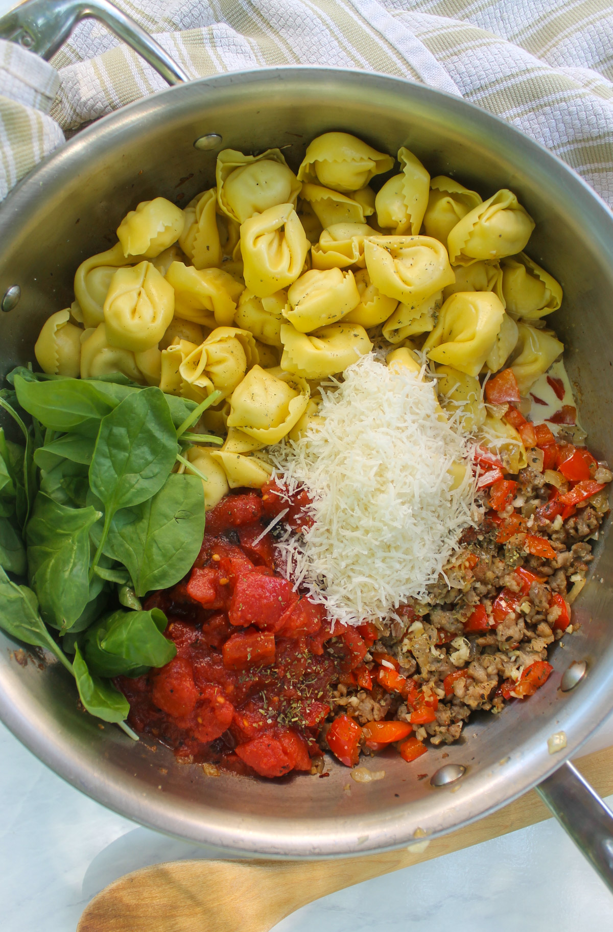 Adding tortellini, crushed tomato, spinach, cream and Parmesan cheese to the skillet with the sausage and veggies.