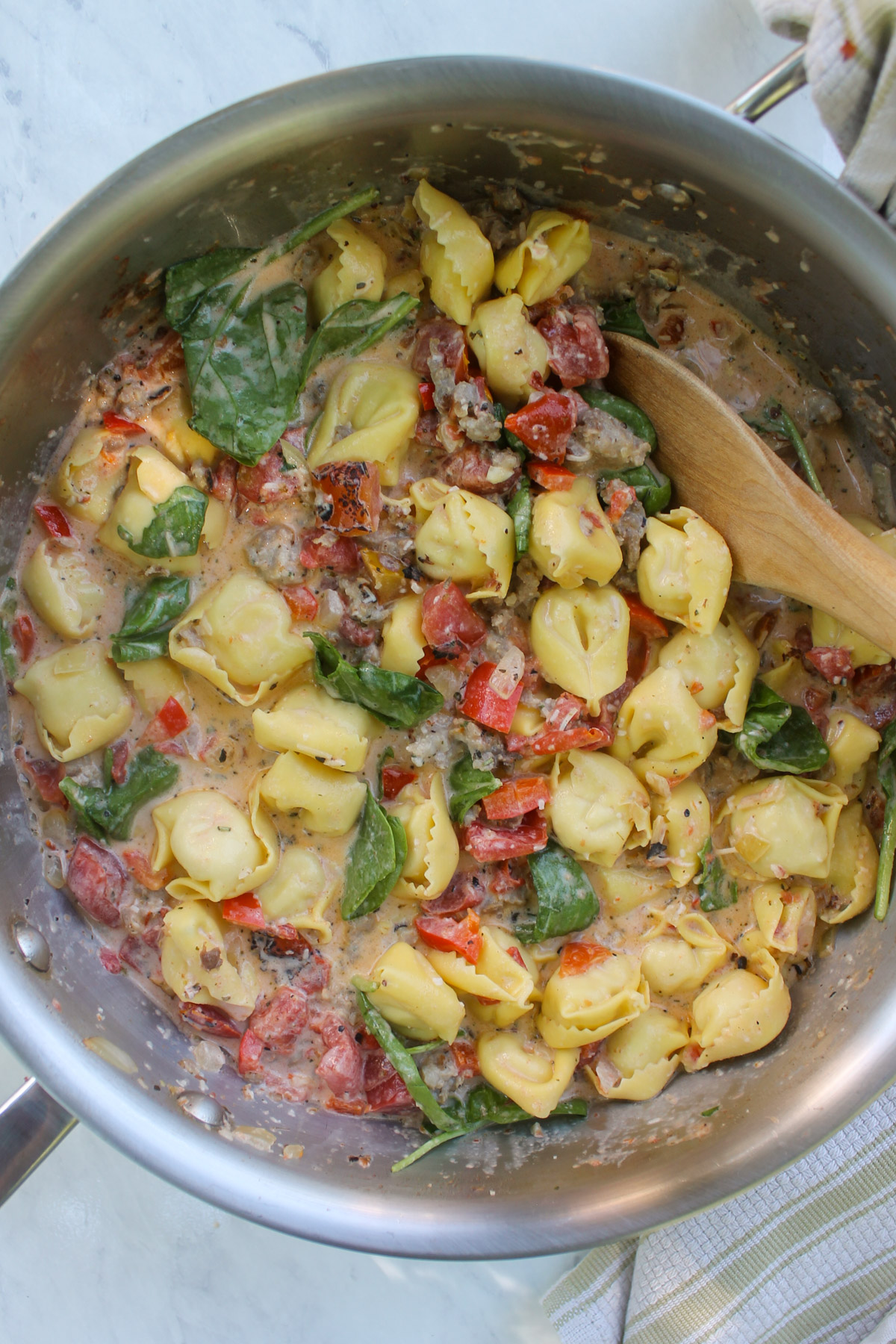 Mixing everything in the skillet together to form a pink sauce with the tortellini.