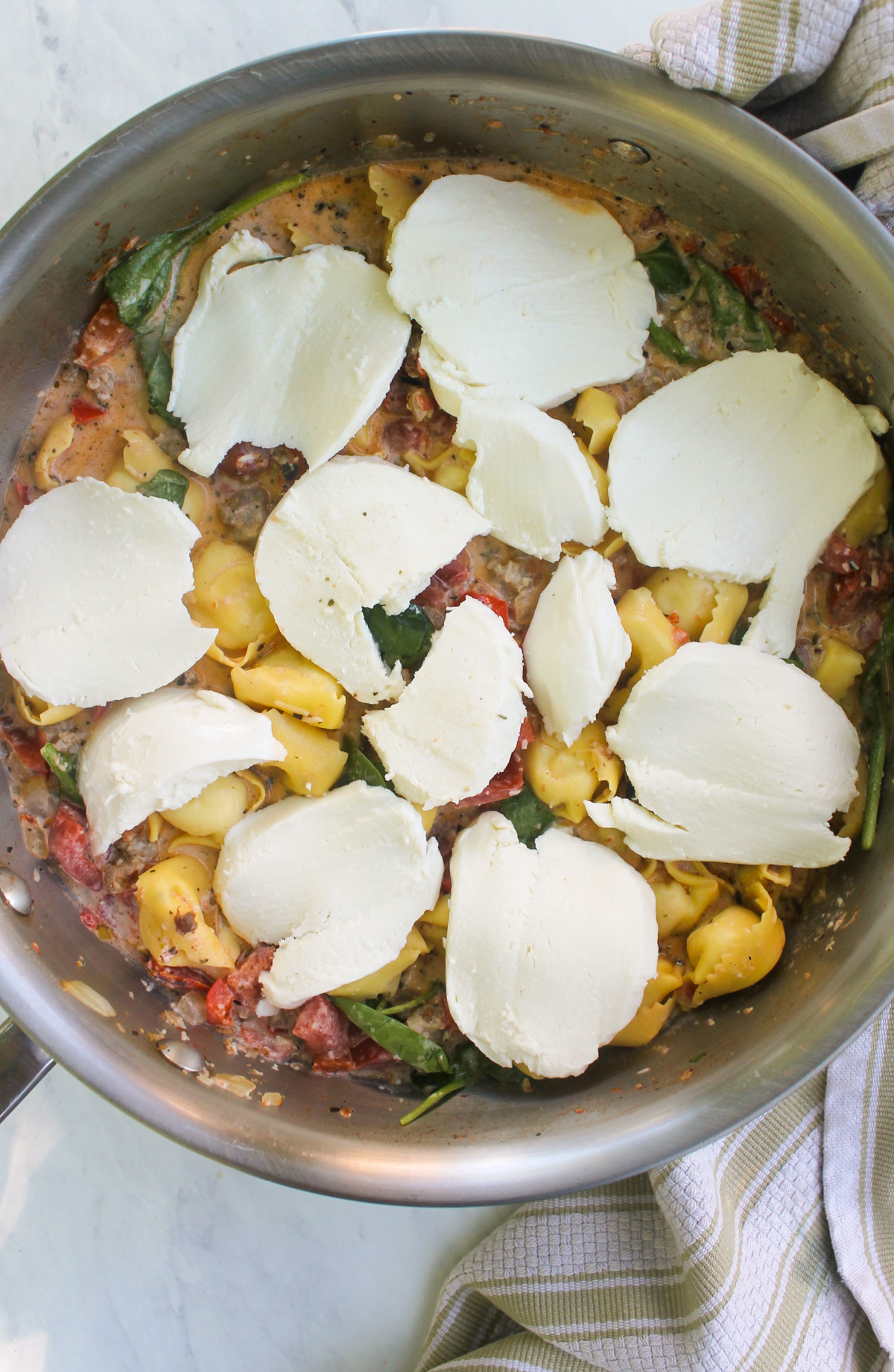 Adding sliced fresh mozzarella cheese to the tortellini skillet to bake.