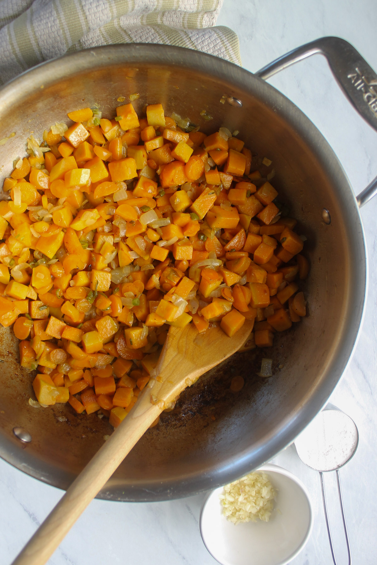 Sauteing sweet potato, onion, carrot and celery in a skillet with a wooden spoon.