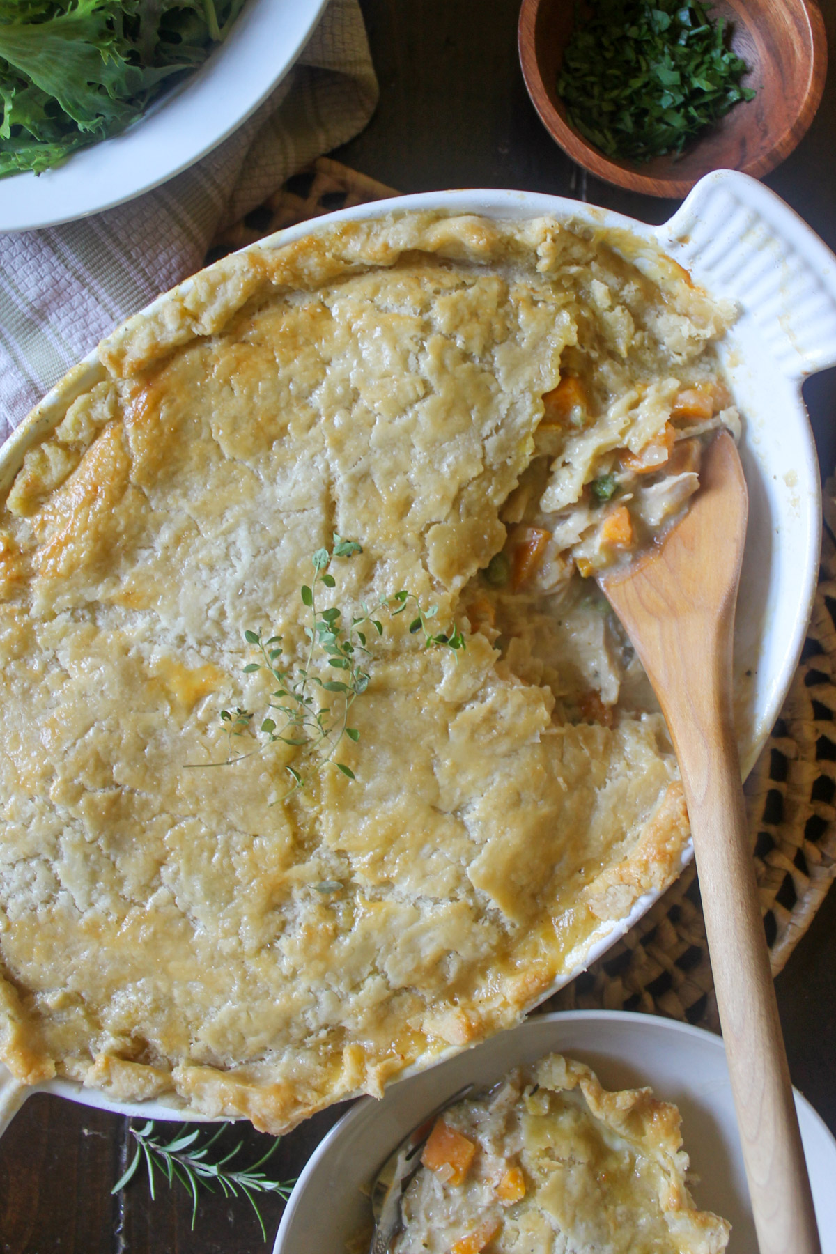 A white oval baking dish of chicken veggie pot pie being served with a wooden spoon.
