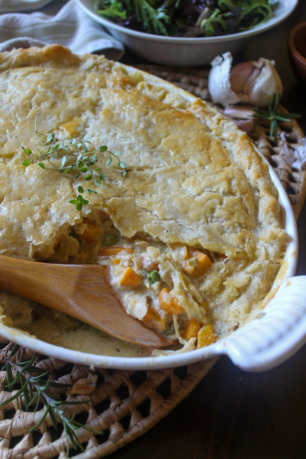 A casserole dish of chicken veggie pot pie broken into with a wooden spoon.