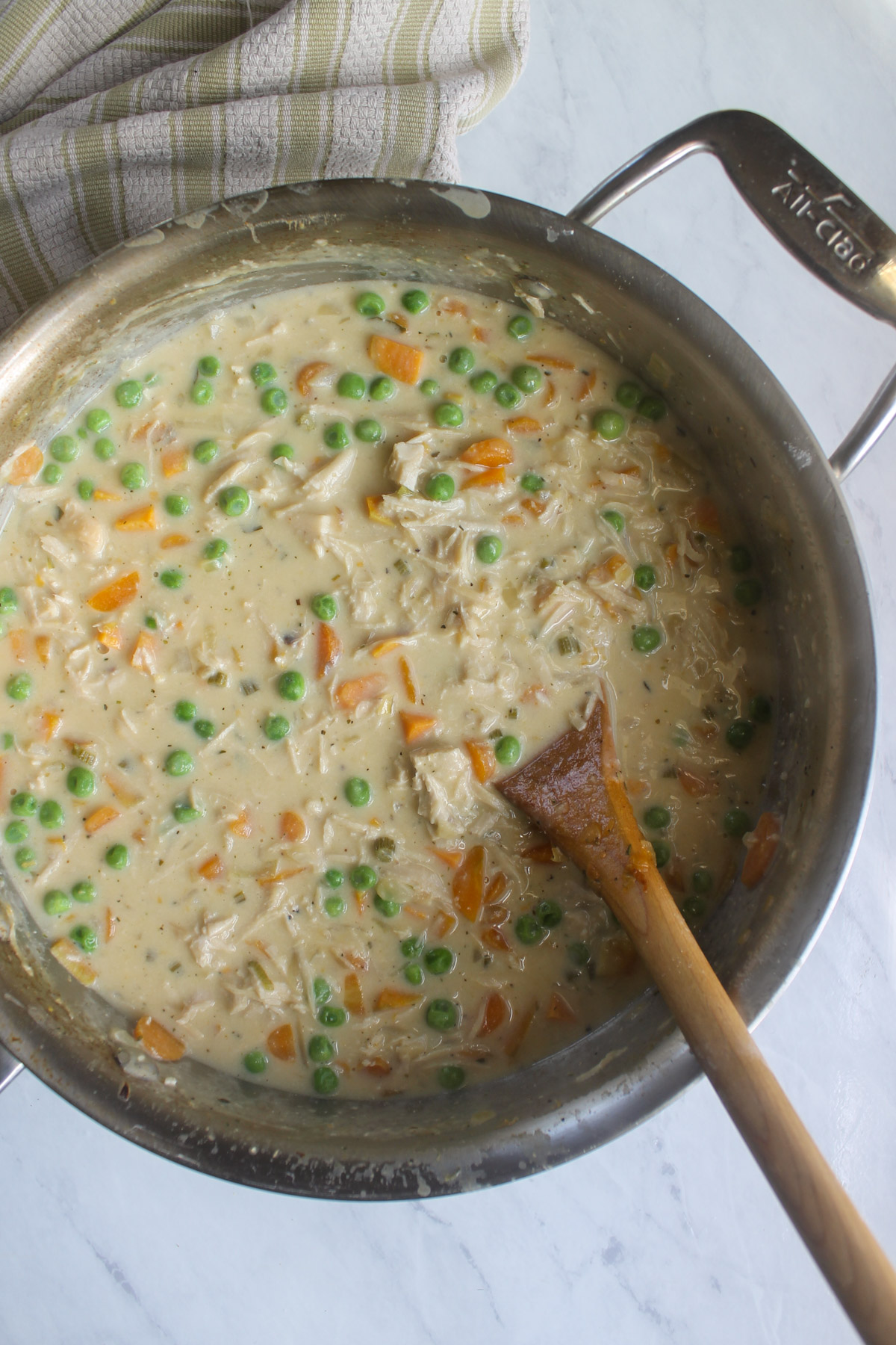Chicken veggie pot pie creamy filling in a skillet with a wooden spoon.