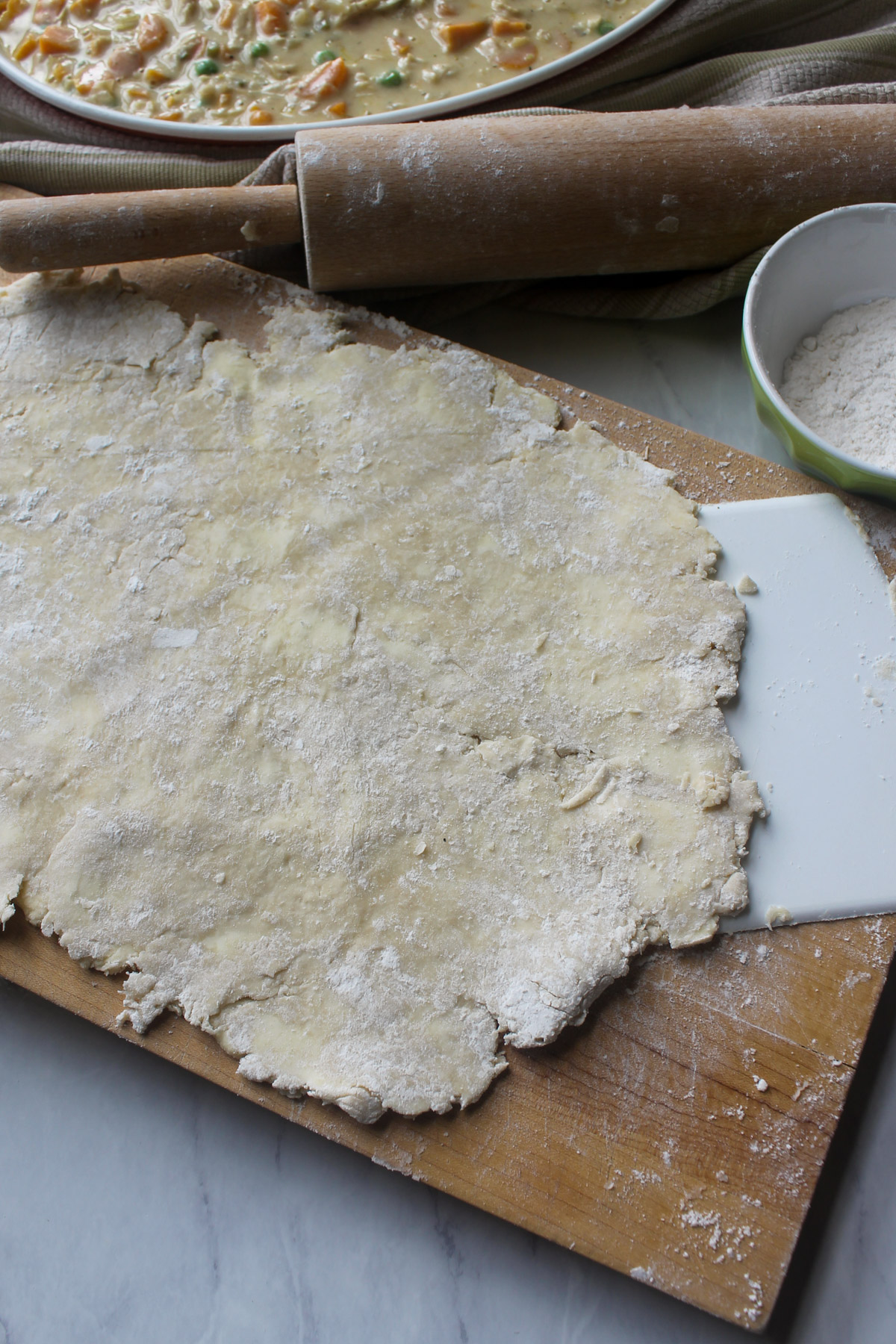 Pie crust rolled out on a cutting board with a rolling pin.