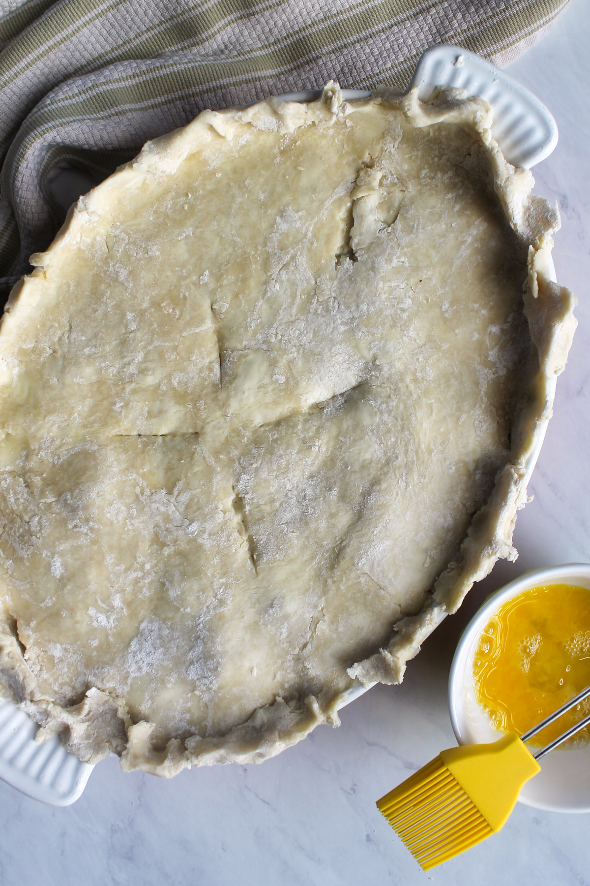 Pie crust on the baking dish of pot pie filling with a bowl of egg wash next to it.