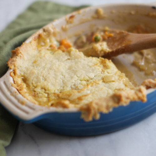 A blue oval baking dish of chicken pot pie that half has been served.