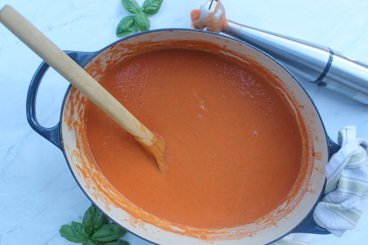 A pot of Tomato Soup blended until smooth with an immersion blender next to the pot.