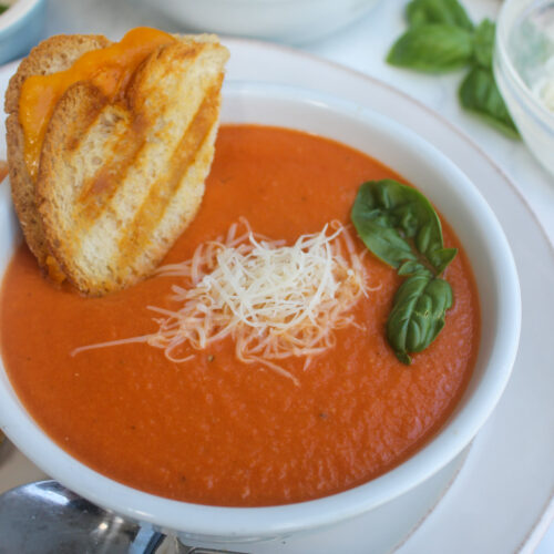 Creamy Tomato White Bean Soup in a bowl topped with Parmesan cheese and basil with grilled cheese.