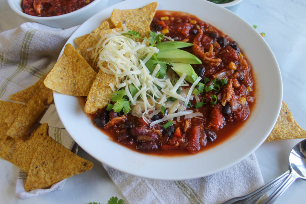 A bowl of Southwest Chicken Chili with tortilla chips and toppings.