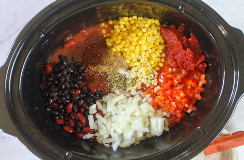 Adding beans, corn, veggies and spices to the crockpot for southwest chicken chili.