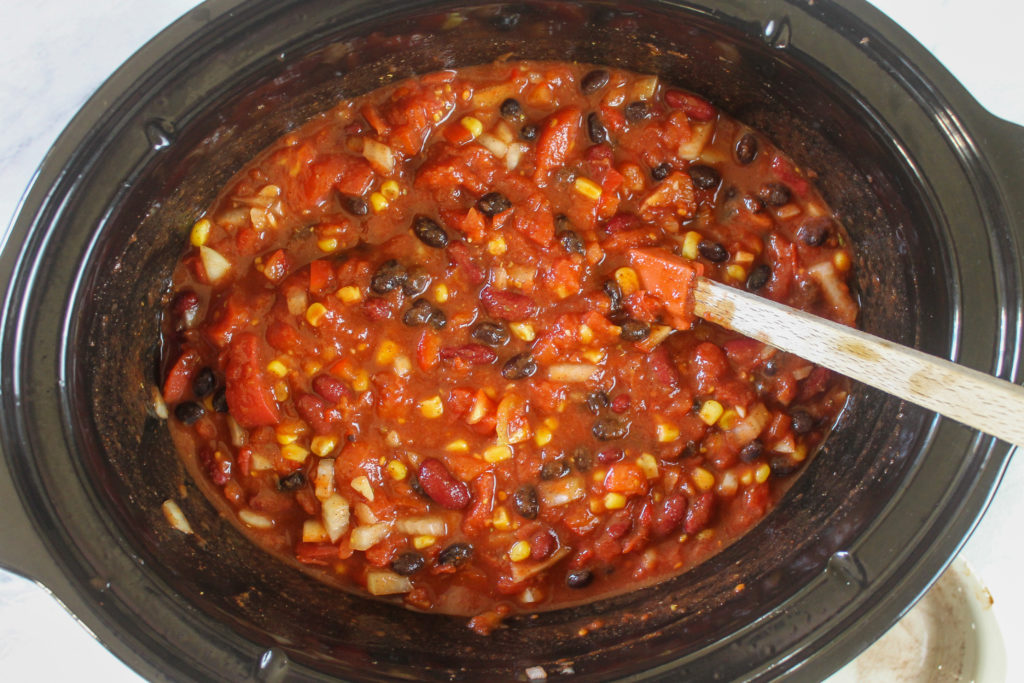 Stirring chili ingredients in a crockpot before the raw chicken is added.