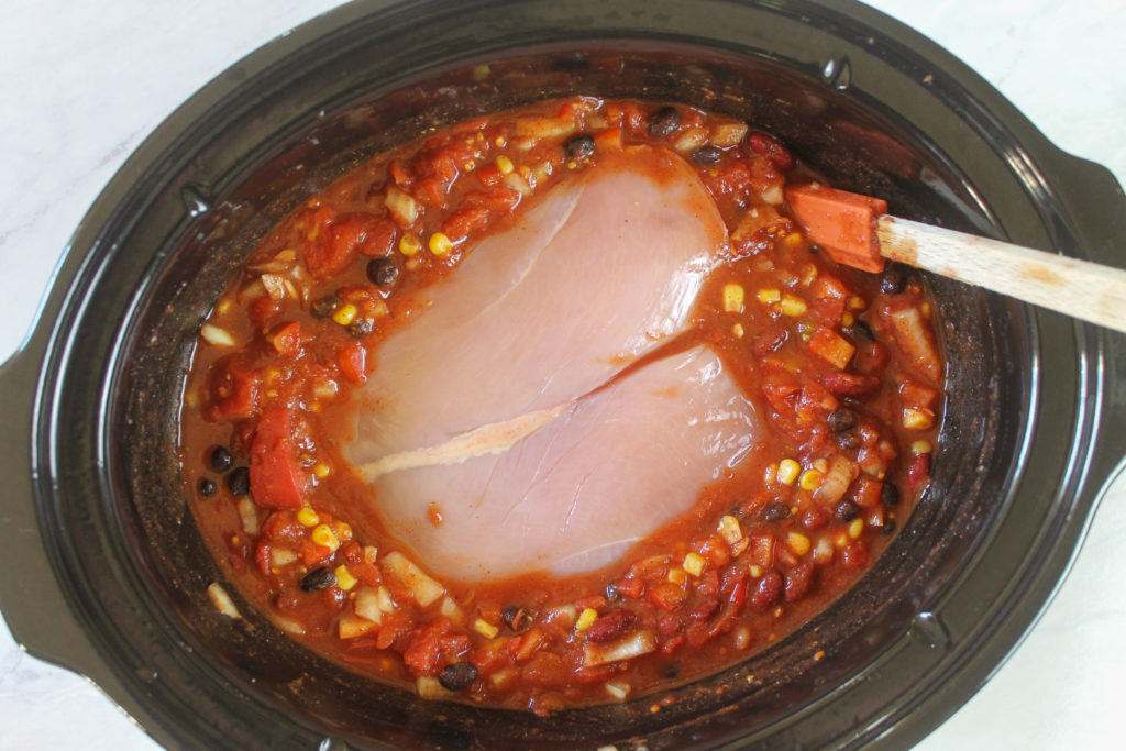 Adding raw chicken breasts to a crockpot of southwest chili to slow cook all day.