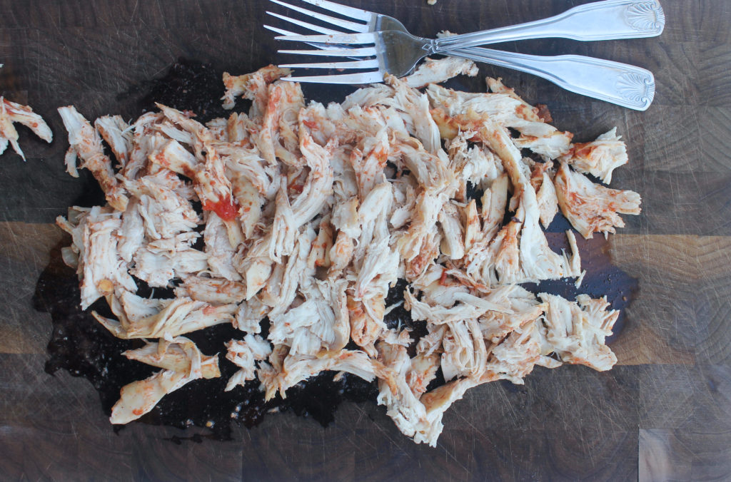 Shredding the chicken on a cutting board with two forks.