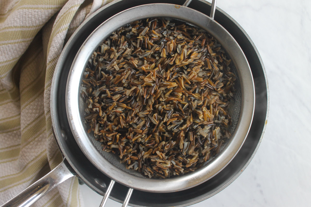 Wild rice cooked separately and sitting in a strainer over a pot to add to soup.