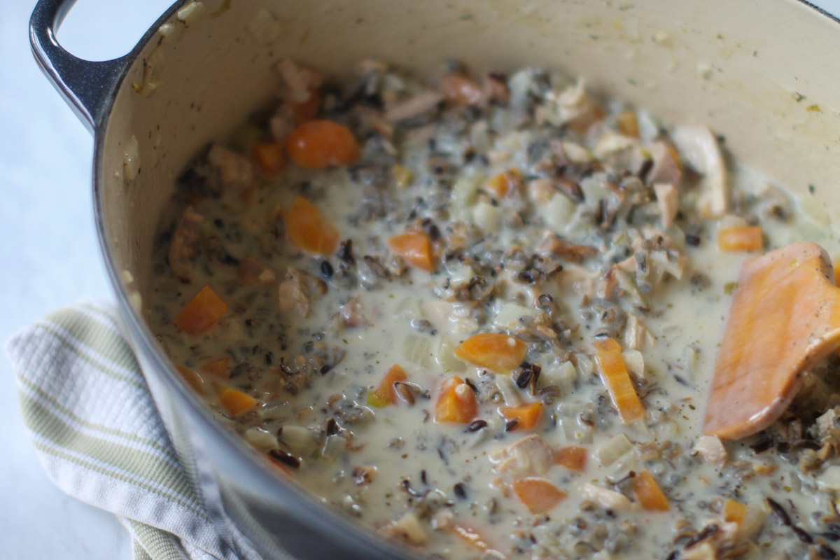 A soup pot of creamy wild rice soup with carrots, onions, chicken and wild rice.