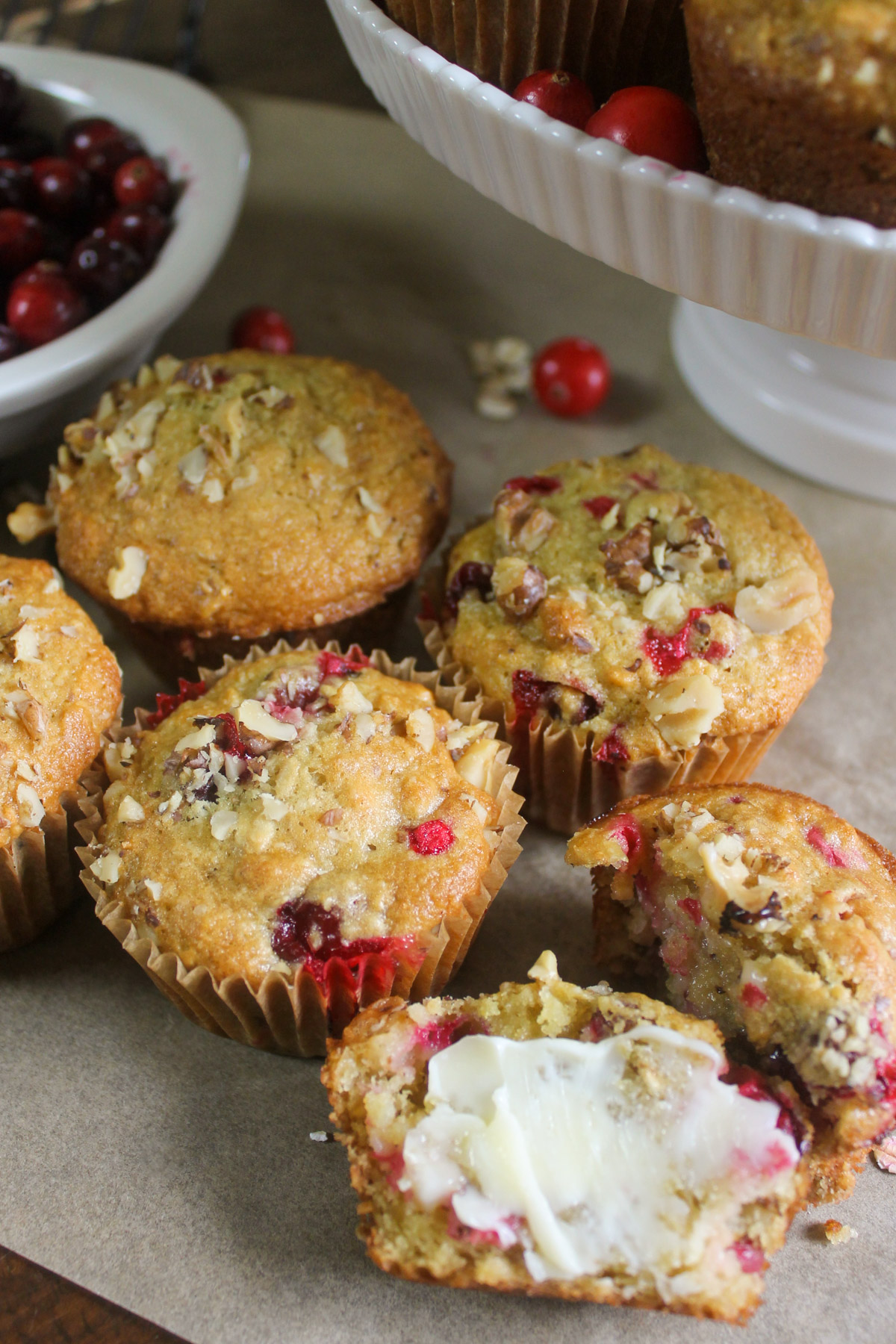 Cranberry muffins on parchment paper under a white cake stand with more muffins.
