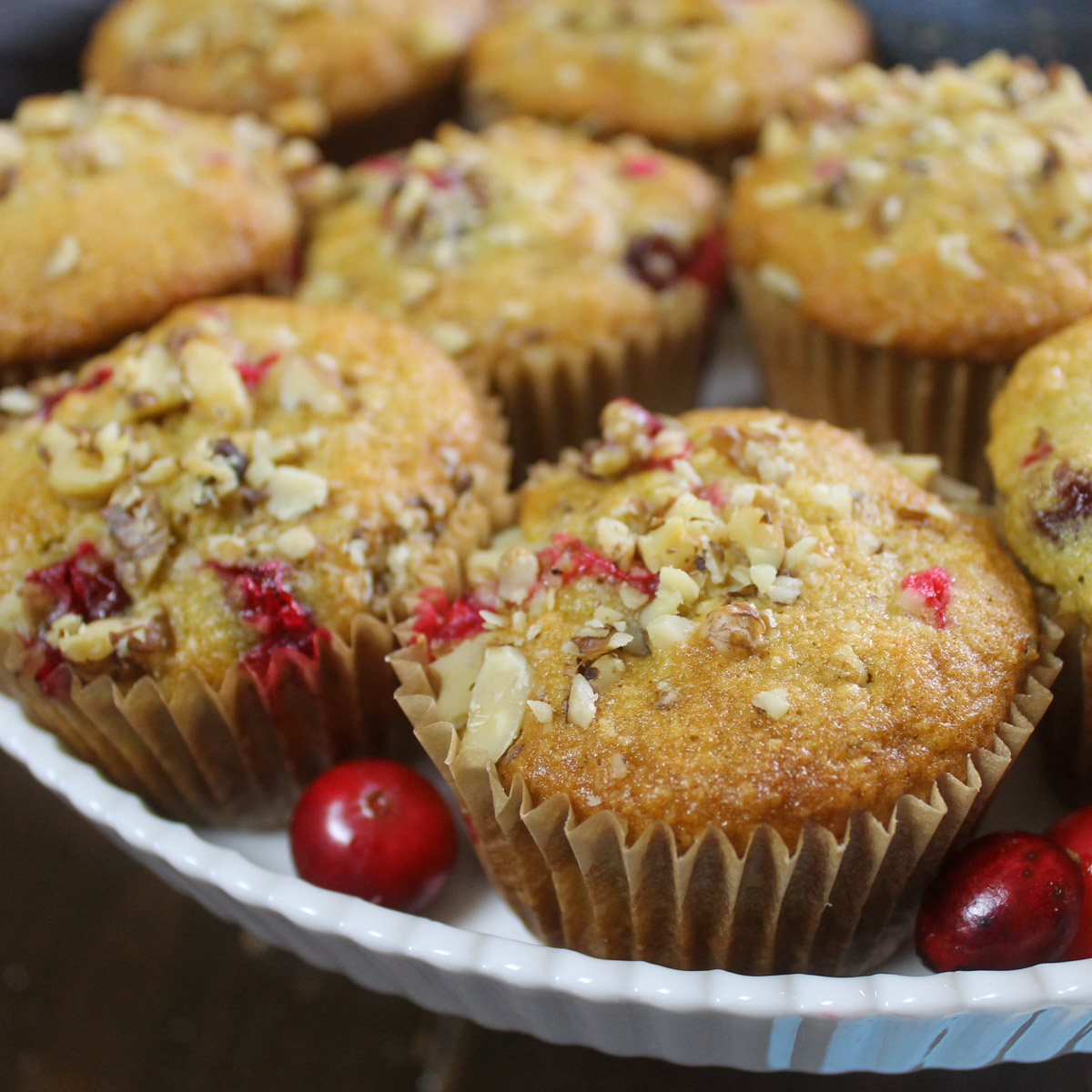 A white cake stand with cranberry muffins with walnut topping.