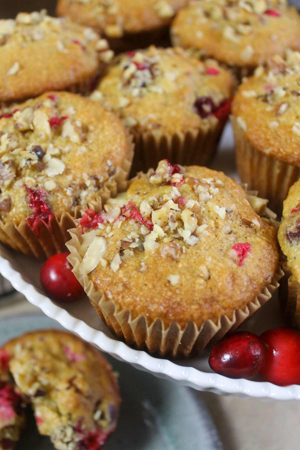A white cake stand with fresh cranberry muffins and bright red cranberries around them.