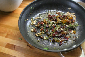 A saute pan of raisin pine nut topping for the goat cheese appetizer.